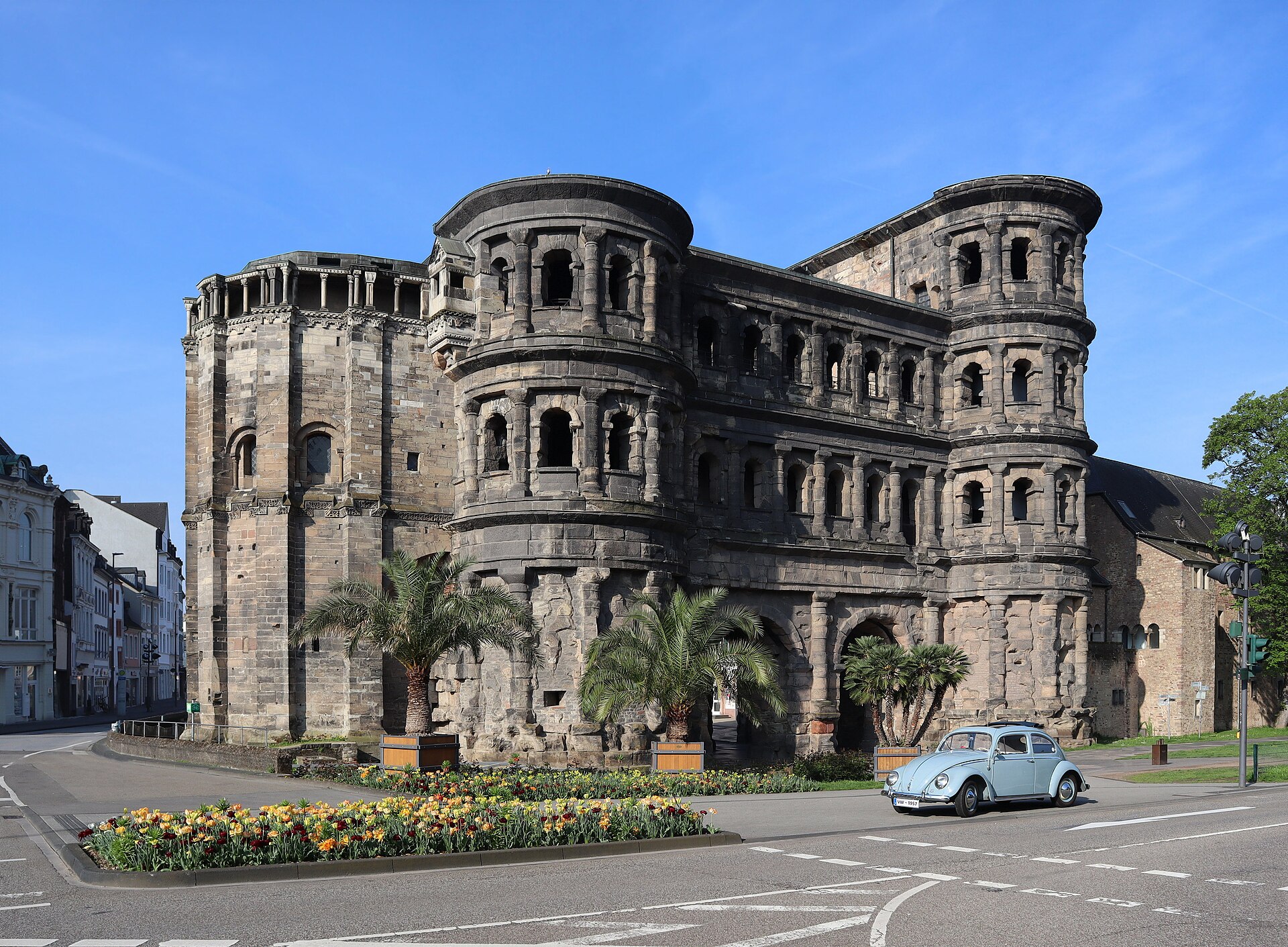 A pale blue 1957 Volkswagen Beetle in front of the Porta Nigra in Trier